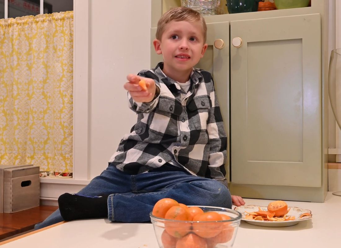 dečak guli mandarine i pruža nekome iza kamere