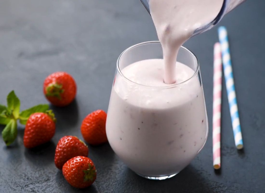 prikaz osobe koja sipa smuti u času, pored jagode i slamčice